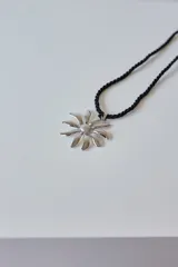 Collar con tiento trenzado color crema y dije de acero quirúrgico hipoalergénico con forma de sol o flor estilizada.