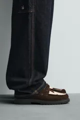 Zapato tipo náutico con diseño de paneles combinados en gamuza marrón y piel con pelo con estampado de vaca. Presenta cordones, horma redonda y suela gruesa con piso track.