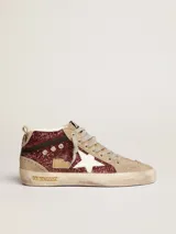 Zapatilla de caña media Golden Goose modelo Mid Star con upper cubierto de glitter color rojo oscuro/bordó. Presenta paneles en gamuza color beige claro y estrella lateral en cuero blanco. La suela tiene un efecto desgastado intencional.