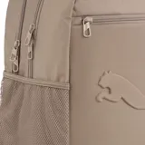 Mochila Puma modelo Buzz Backpack color marrón claro con base negra. Cuenta con dos compartimentos principales con cierre, un bolsillo frontal con cierre, bolsillos laterales de red y correas ajustables acolchadas. Incluye el logo de la marca en relieve en el frente.