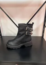 Botas cortas de cuero vegano color negro, con suela track gruesa y dos correas laterales con hebillas metálicas decorativas.