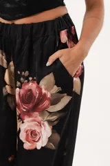 Pantalón palazzo negro con estampado floral en tonos rosa, naranja y amarillo. Tiene cintura alta con elástico.
