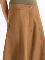 Pollera midi de silueta en A color marrón, con bolsillos ocultos en los laterales, recortes verticales y cierre frontal con botón personalizado.