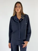 Chaqueta tipo camisa de denim color borgoña, con cuello clásico, manga larga, cierre frontal con botones y bolsillo de parche en el pecho.