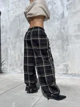 Pantalón de corte holgado y silueta tipo barrel, confeccionado en tela viyela con estampado de cuadrillé en tonos negro, beige y líneas finas rojizas. Presenta cintura elástica y puños ajustados en el tobillo.