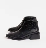 Bota corta de cuero vacuno negro con textura de reptil, punta cuadrada y taco cuadrado de madera. Cuenta con cierre lateral interno y suela de caucho.