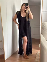 Chaleco largo sin mangas, tejido en punto calado tipo red con hilo de algodón y lurex, color marrón. Presenta escote profundo en V, tiras para atar en el frente, tajo trasero y flecos en el ruedo.