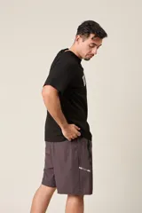 Bermuda deportiva color verde militar, de corte suelto, con cintura elástica y cordón de ajuste. Cuenta con detalles de líneas verticales en los costados y bolsillos laterales con cierre.