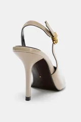 Zapato de tacón alto color beige, tipo destalonado, con punta fina y tira trasera con hebilla ajustable. Tacón fino de 9 cm de altura.