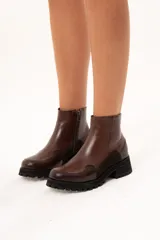 Bota de cuero color chocolate con caña al tobillo y cierre lateral. Presenta una combinación de texturas en el cuero y una suela chunky dentada de color negro.