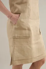 Vestido midi de lino color beige, de silueta relajada, escote redondo, sisas amplias y bolsillos delanteros aplicados.