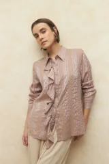 Camisa color beige con estampado de rayas verticales y textura cuadriculada. Tiene cuello clásico, mangas largas con puños abotonados, cierre frontal con botones de nácar y volados verticales en el frente.