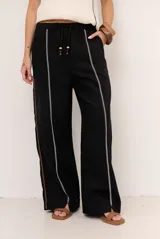Pantalon de lino color marrón con costuras blancas decorativas a lo largo de las piernas y corte amplio.