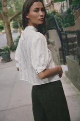 Blusa blanca de cuello alto con detalles de puntilla, manga corta abullonada y cierre posterior con botón.