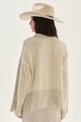 Sweater de tejido de punto en color beige, con mangas largas que presentan detalles de textura en relieve y paneles laterales en tono gris. Confeccionado en lana italiana, cuenta con puños acanalados y detalles en lurex.