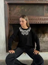 Remera negra de mangas largas con cuello redondo y bordado blanco en el escote.
