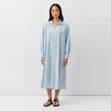 Vestido camisero midi celeste con finas rayas, cuello camisero, escote en V con botonadura frontal, bolsillos en el pecho, mangas largas anchas y aberturas laterales.