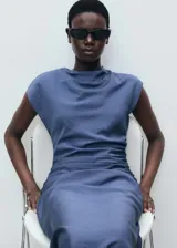 Vestido midi de color azul, con cuello drapeado, diseño sin mangas y detalle de drapeado en la cintura. Presenta un corte recto y cierre de cremallera lateral.