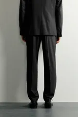 Pantalón de traje slim fit para hombre, color gris oscuro, con bolsillos frontales y bolsillos traseros de doble vivo con botón. Cuenta con cierre frontal de cremallera y botón, y presillas para cinturón.