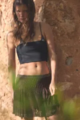 Falda corta de tiro medio confeccionada en tejido de encaje color marrón, con diseño evasé y detalle de aplicación de tachas metálicas en la cintura y el ruedo.