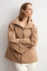 Trench color camel con capucha desmontable, cierre frontal con cremallera, bolsillos laterales y mangas largas con ajuste en puños.
