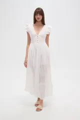 Vestido largo blanco de algodón con escote en V, manga corta con volados de broderie y talle entallado con botones frontales. La falda es amplia y presenta detalles de bordados calados en el ruedo.