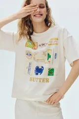 Remera oversized de punto suave de algodón, color blanco, con cuello redondo acanalado, hombros caídos y bajo recto. Presenta un diseño estampado al frente con ilustraciones de diferentes marcas y envases de manteca.