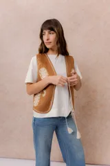 Chaleco corto de efecto gamuza en color tostado, con bordados decorativos en contraste y terminaciones bordadas en los bordes. Presenta escote en V y diseño recto.