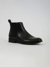 Botin tipo Chelsea de cuero sintético negro, con paneles laterales elásticos, tirador trasero y suela de goma dentada.