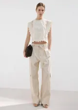 Top blanco de algodón con cuello redondo, detalles bordados, inserciones de encaje y terminaciones festoneadas en mangas y ruedo.