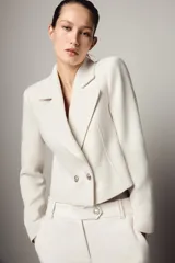 Blazer corto de cuello solapa y manga larga con hombreras. Presenta un diseño cruzado con cierre frontal de dos botones dorados.
