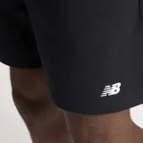 Short deportivo negro de algodón y poliéster reciclado, con cintura ajustable con cordón, bolsillos laterales y bolsillo trasero. Logo de New Balance estampado en blanco en la pierna izquierda.
