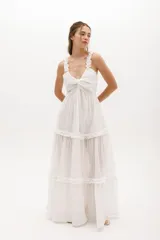 Vestido largo blanco de gasa de algodón con textura liviana. Tiene escote en V con nudo central, breteles con voladitos y falda con frunces.