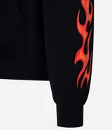 Buzo con capucha negro de corte oversized, con bolsillo canguro y cordones ajustables. Presenta un estampado frontal con una calavera y la palabra 'FEARLESS' envuelta en llamas naranjas y rojas, diseño que se repite en las mangas.