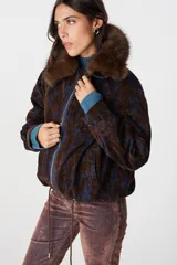 Campera de corte bomber con estampado abstracto en tonos marrón chocolate y azul. Presenta cuello de piel sintética desmontable, cierre frontal metálico, puños de tejido acanalado en color azul y cordón ajustable en el ruedo.