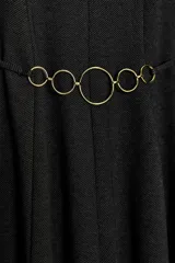 Vestido corto de cuello redondo y sin mangas, confeccionado en tela de sarga color gris oscuro. Presenta un diseño entallado en el torso con falda evasé y un cinturón integrado con arandelas metálicas doradas en la cintura. Cierre posterior con cremallera oculta.