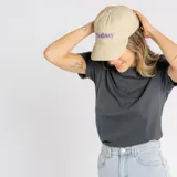 Gorro tipo cap color beige con visera curva y bordado frontal con la palabra 'Holiday' en color violeta.