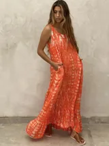 Vestido largo sin mangas con estampado tie-dye en tonos naranja y blanco. Presenta un corte holgado, bolsillos laterales y un detalle de volado en el ruedo.