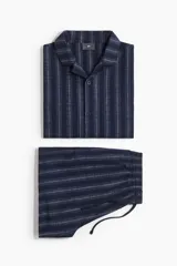 Conjunto de pijama de dos piezas compuesto por una camisa de manga corta con cuello abierto y botones, y un short con cintura elástica y cordón de ajuste. Presenta un diseño a rayas verticales en tonos azul marino.