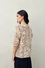 Blusa color beige con estampado abstracto en blanco, corte relajado, mangas 3/4 fruncidas y cuello con volados.