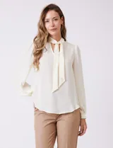 Blusa de gasa color crema, marca Zac & Rachel, con escote en V y lazo para anudar en el cuello. Mangas largas con puños abotonados.