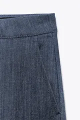 Pantalón de tiro alto confeccionado en algodón, con corte recto y diseño minimalista. Presenta bolsillos laterales, raya planchada en el delantero y cierre frontal con cremallera, botón y ganchos metálicos.