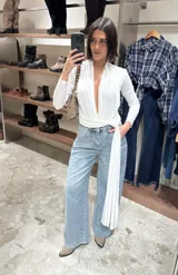 Body de manga larga en color blanco, con escote profundo en V y diseño cruzado que se anuda en la cintura, dejando una tira larga colgante.