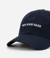 Gorra de sarga color negro con visera curva y bordado frontal en blanco con la frase "NOT YOUR BABE". Cuenta con regulador en la parte trasera.