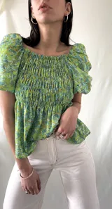 Blusa verde con estampado floral en tonos celeste y marrón, escote cuadrado con elástico, mangas cortas abullonadas y cuerpo fruncido.