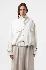 Campera de denim liviano oversize color blanco, con cuello alto, cierre frontal con botones y bolsillos delanteros con solapa. Presenta pespuntes en contraste y una silueta relajada.