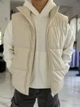 Chaleco puffer de cuerina beige, sin mangas, con cuello alto, cierre frontal y bolsillos laterales.
