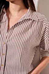Camisa de corte oversize con estampado de rayas verticales en tonos marrón y beige. Presenta cuello camisero, cierre frontal con botones y mangas cortas con caída relajada.