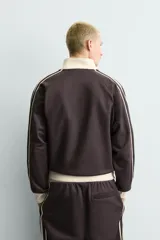 Sudadera de corte relajado en color azul marino con cuello alto y cierre frontal de cremallera. Presenta bandas laterales en color crema a contraste que recorren las mangas, puños y bajo en tejido rib, y bolsillos laterales de vivo.