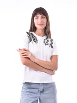 Remera blanca de manga corta con cuello redondo, destacada por apliques bordados con lentejuelas en los hombros.